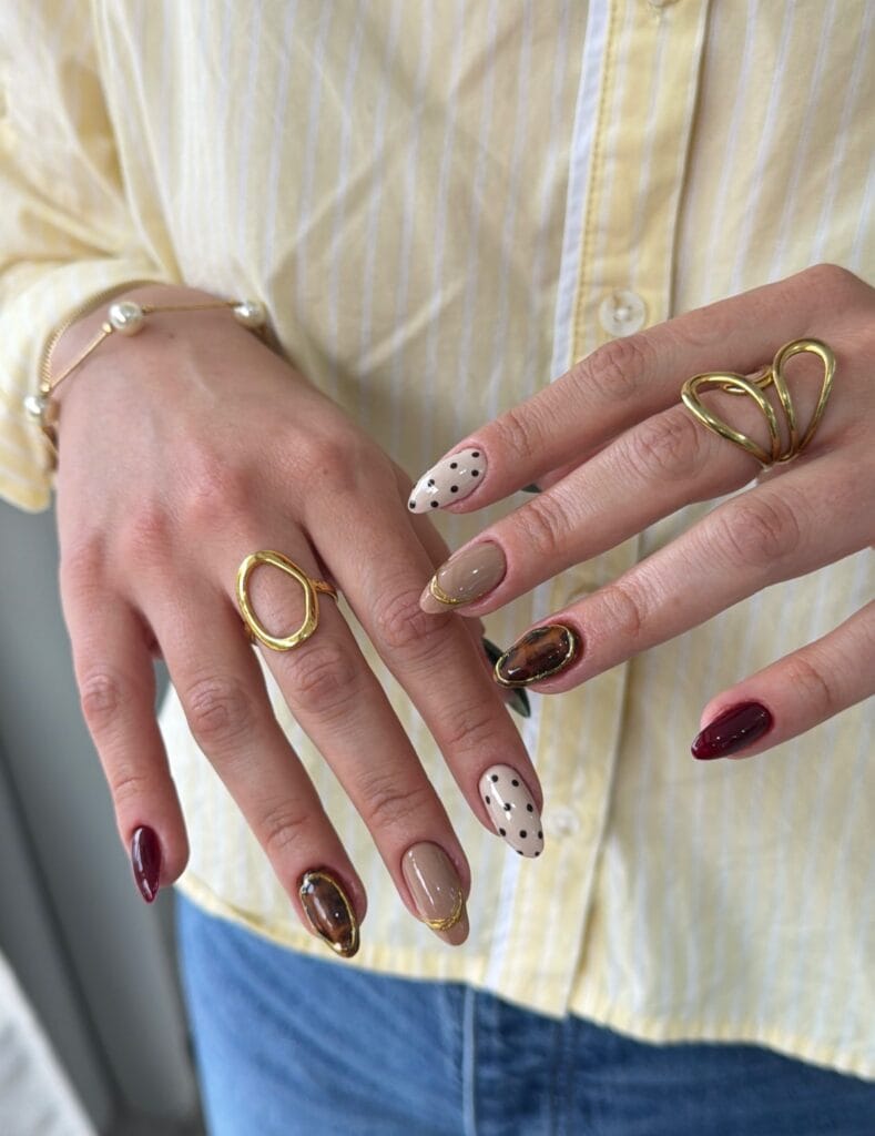Autumn nails with nude polish, black polka dots, tortoiseshell accents, gold outlines, and burgundy nails.
