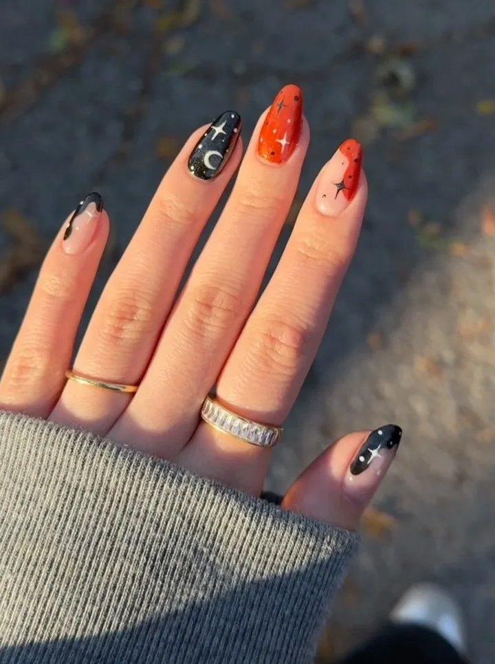 Orange and black Halloween nails with wavy French tips, a crescent moon, and tiny stars over nude accents.