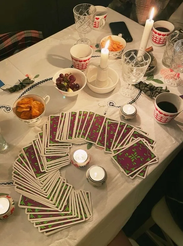 Halloween party tarot card table with candles, snacks, drinks, and a deck of cards spread across the table