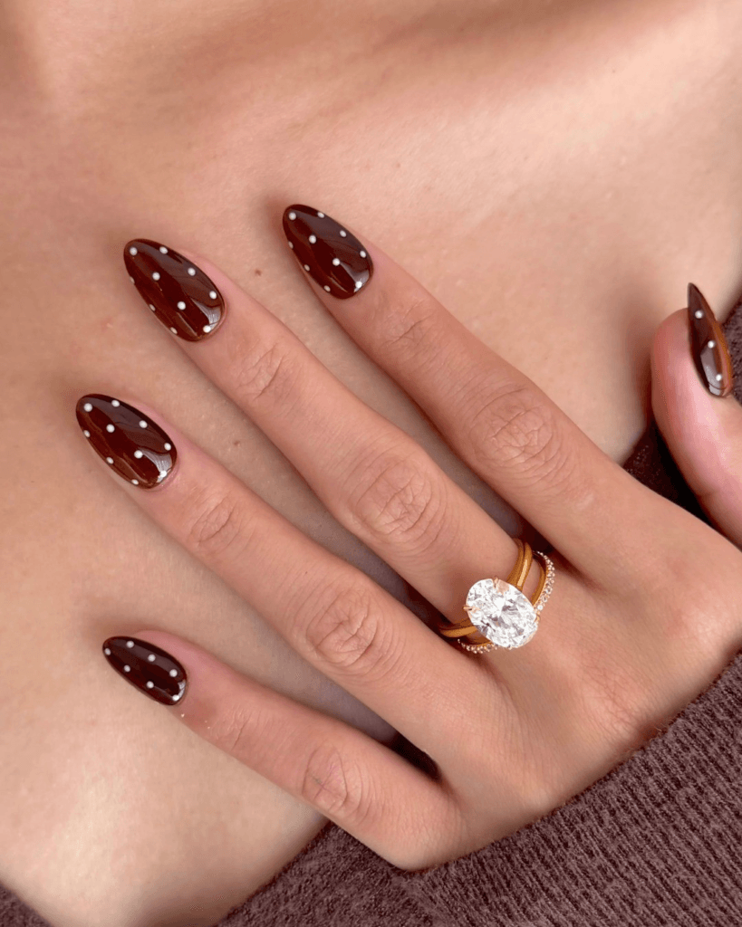 Almond fall polka dot nails with a glossy chocolate brown base and small white dots.
