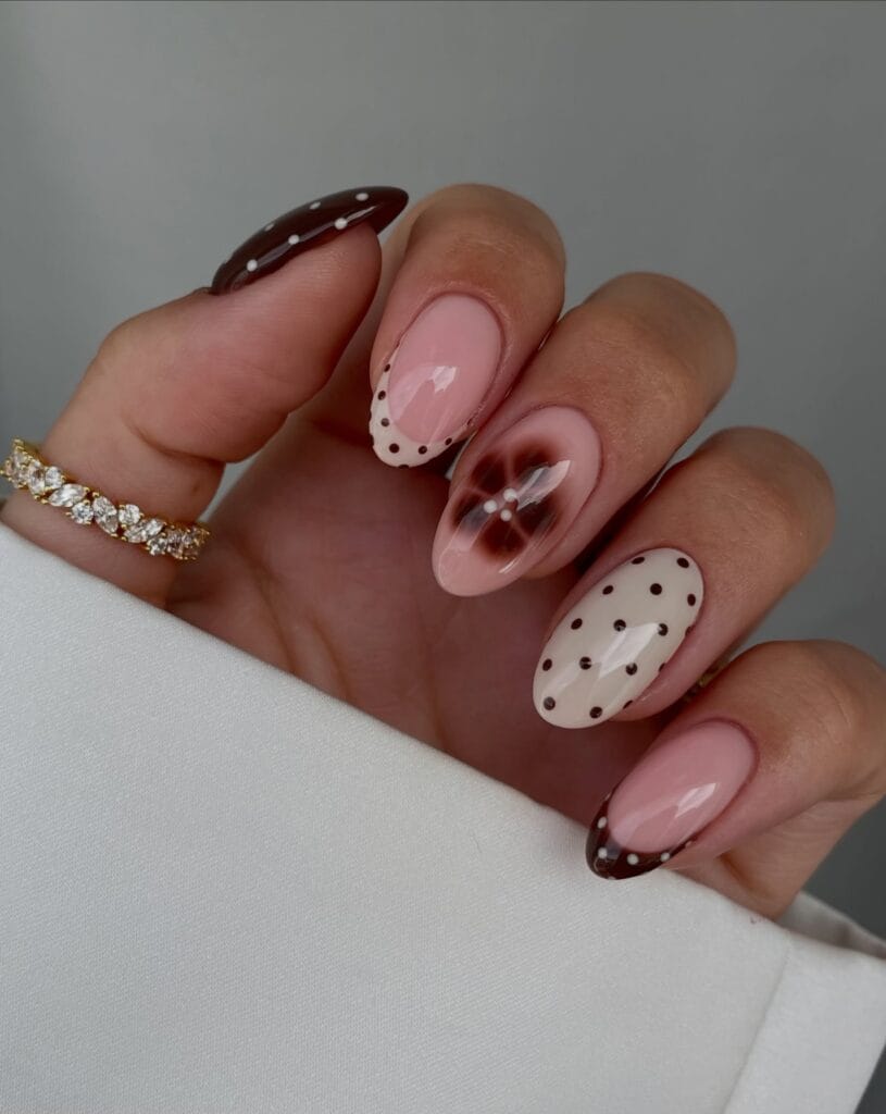 October nails with brown polka dots, dotted French tips, and a blurred brown flower with pearl accents.
