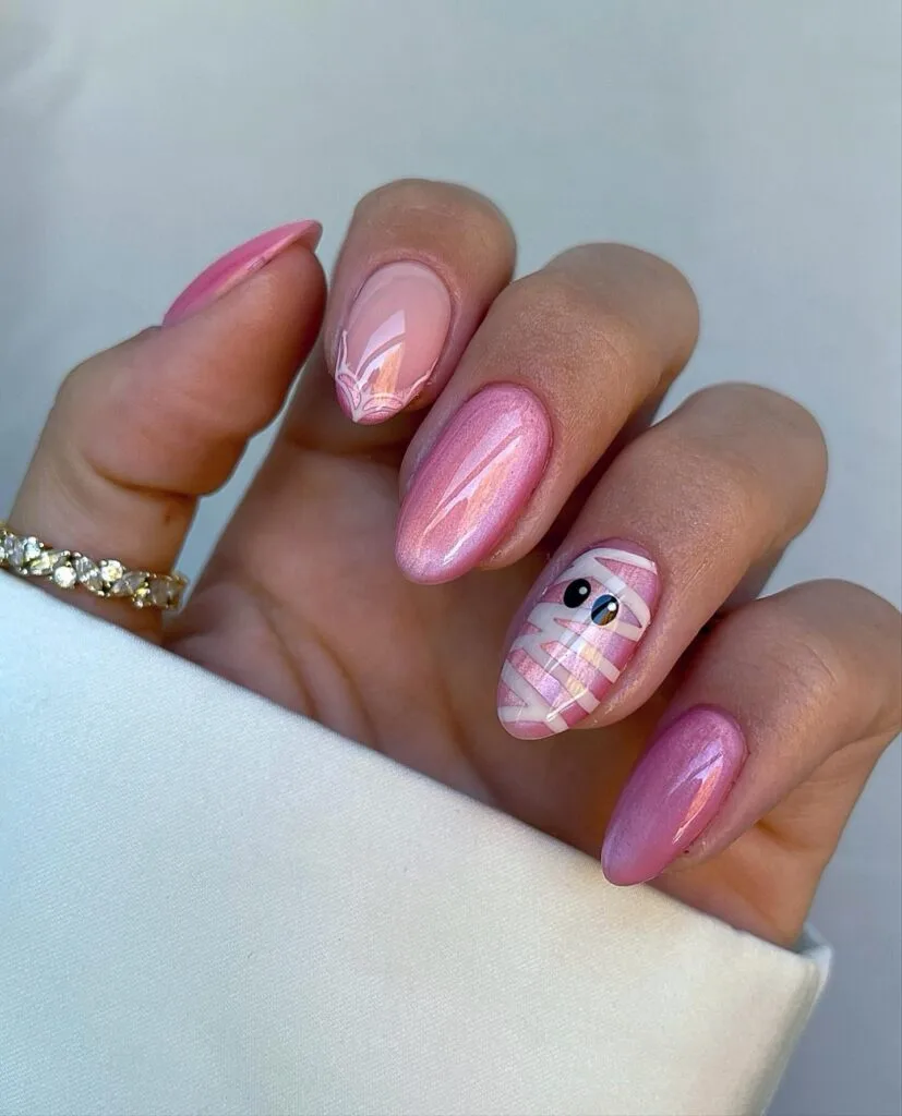 pink Halloween nails with shimmer polish, a mummy accent nail, and a pale web detail