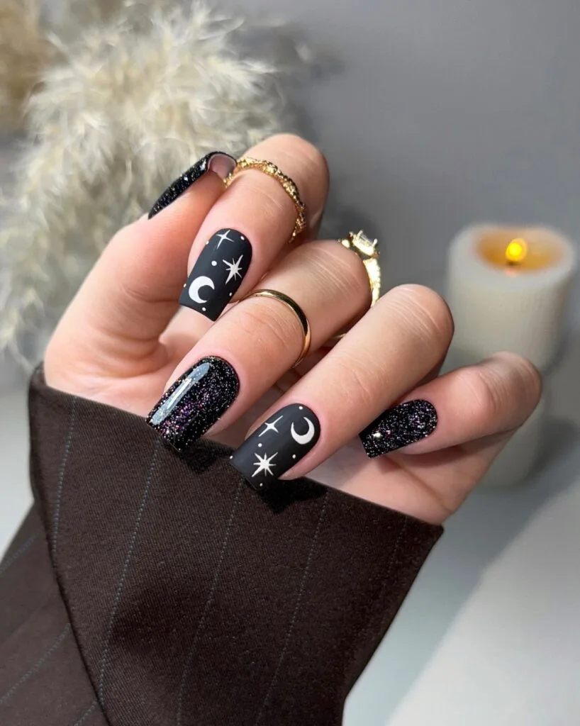 Square black witchy nails alternating matte white moon-and-star art with glossy glitter nails.