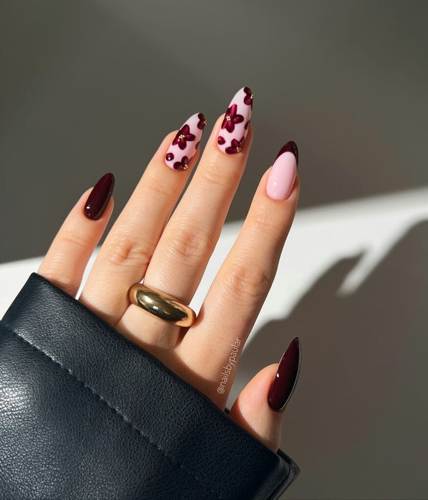 Burgundy fall nails with pink base, floral nail art, and dark French tips on almond nails.
