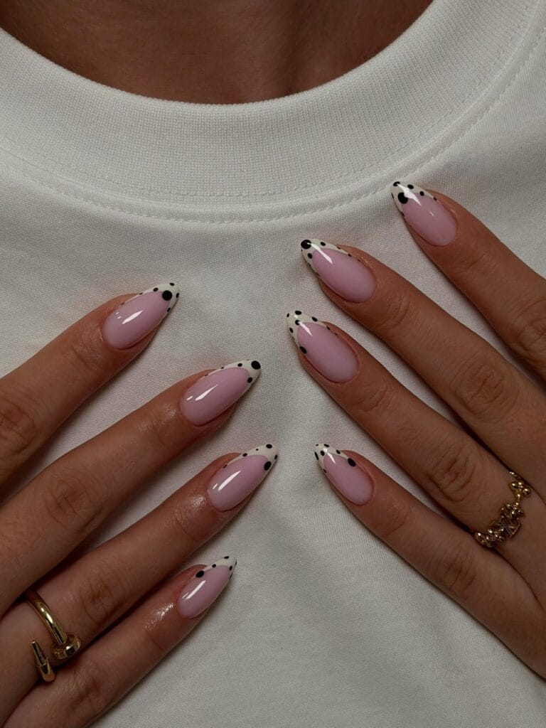 Fall polka dot nails with glossy pink almond bases and cream French tips dotted in different-sized black spots.
