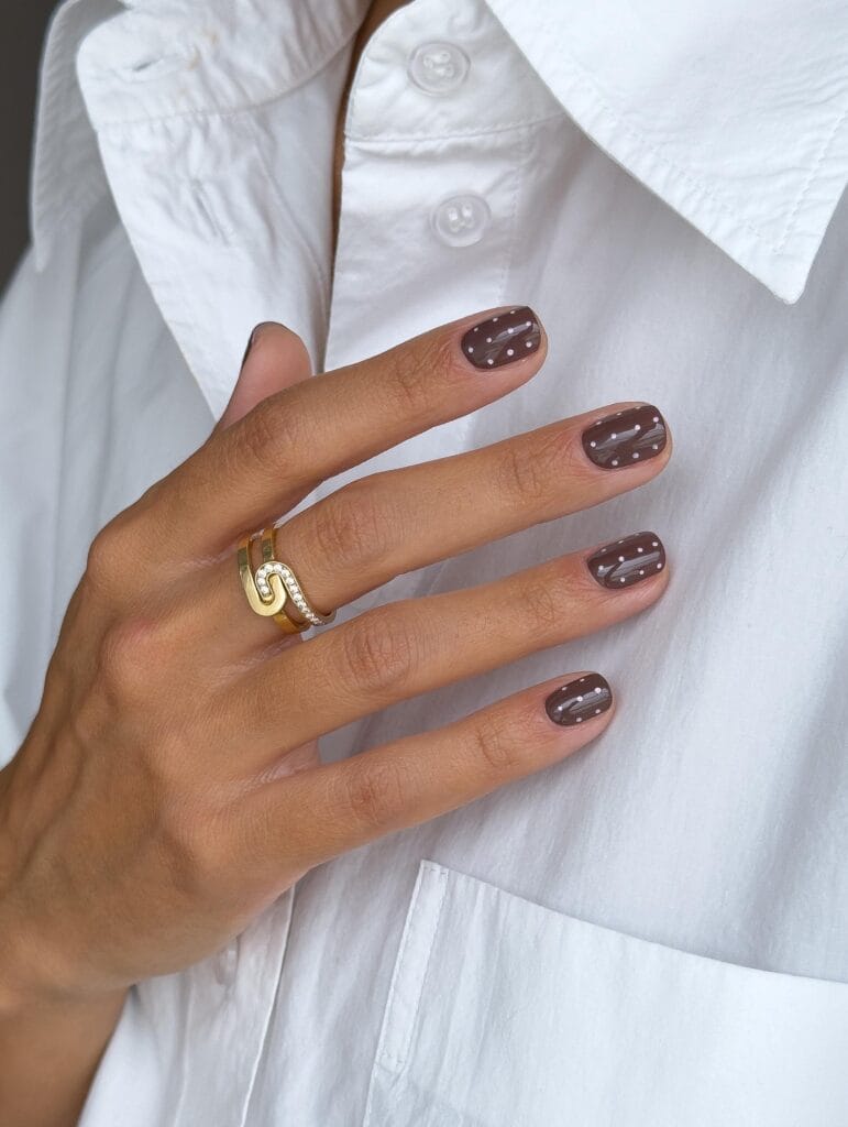 Short autumn nails in taupe brown with tiny white dots and fine white line accents.
