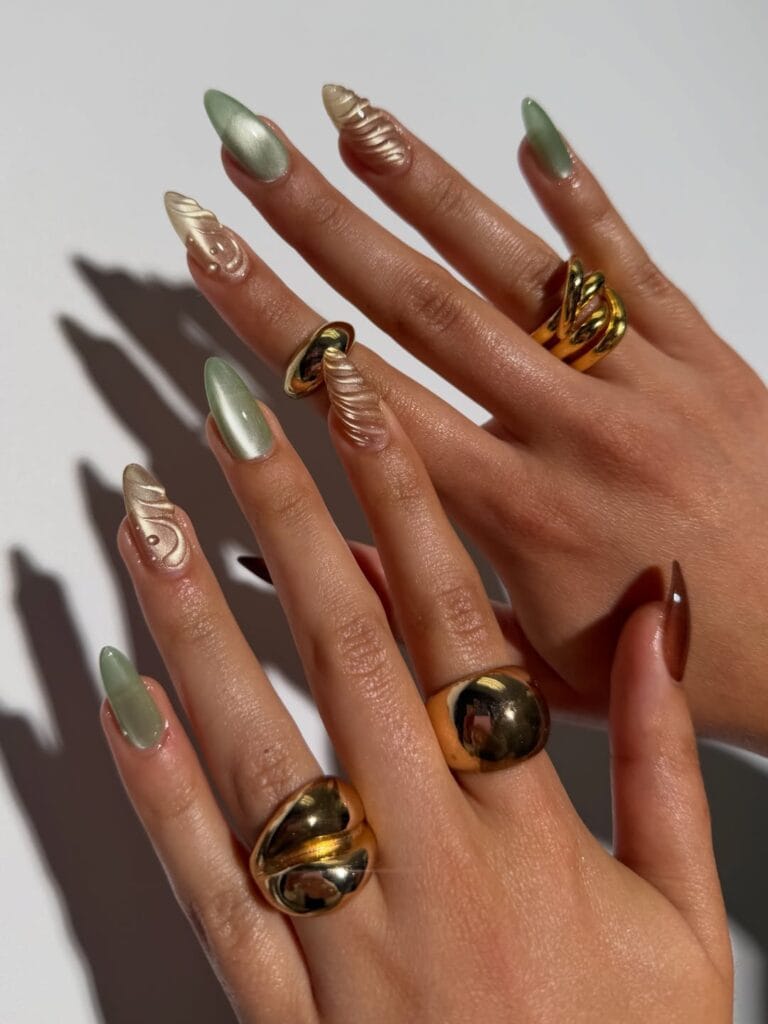 Fall nails with sage green cat-eye polish and pearl chrome 3D swirl nail art on almond nails.
