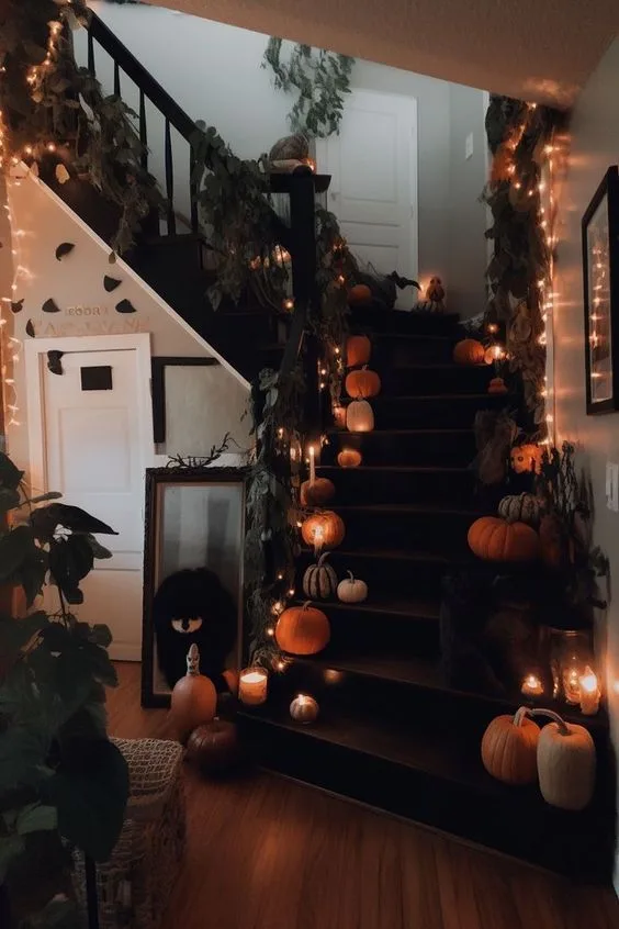 Halloween staircase decor with pumpkins, greenery, and warm string lights on dark steps
