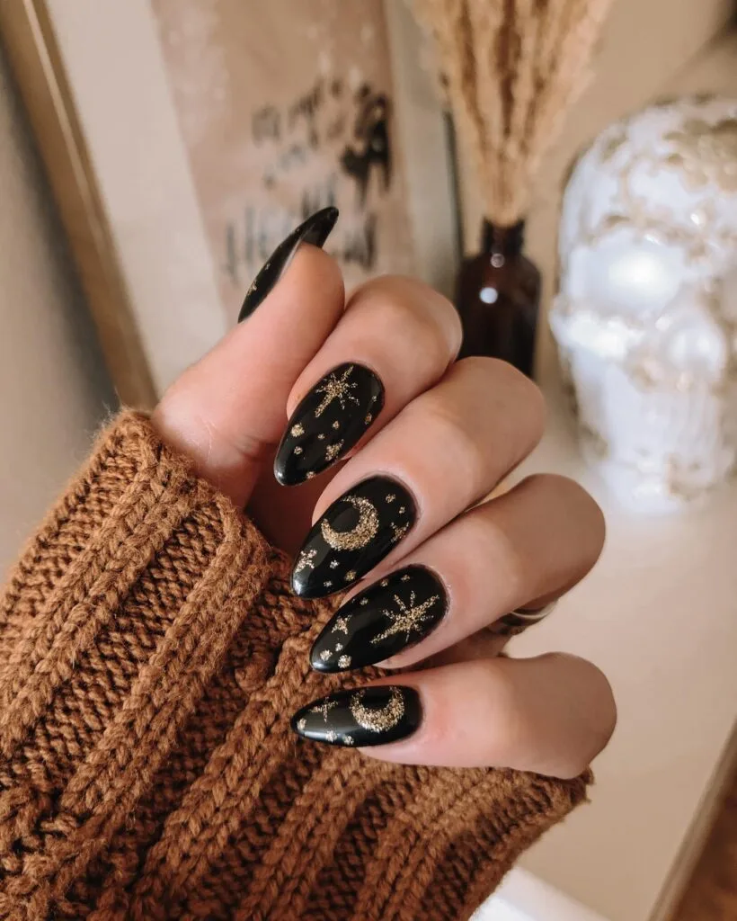 Black almond nails with gold glitter crescent moons, stars, and dots for a celestial witchy manicure.