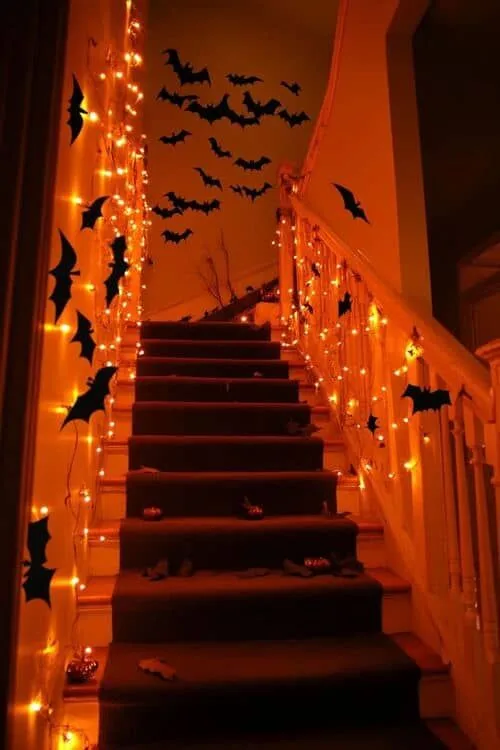 Halloween staircase decor with orange string lights and black bats along the walls and railing
