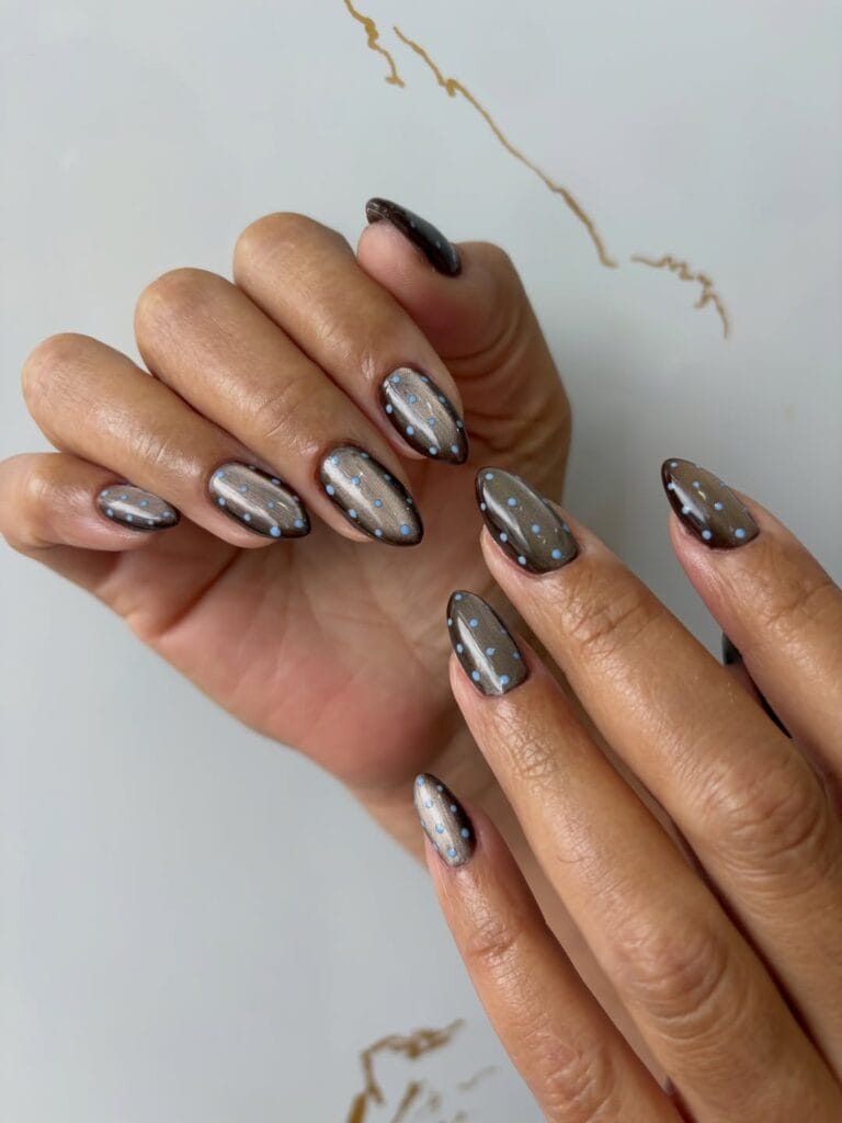 Almond autumn nails with a smoky brown base, silvery metallic sheen, and tiny pale blue polka dots.
