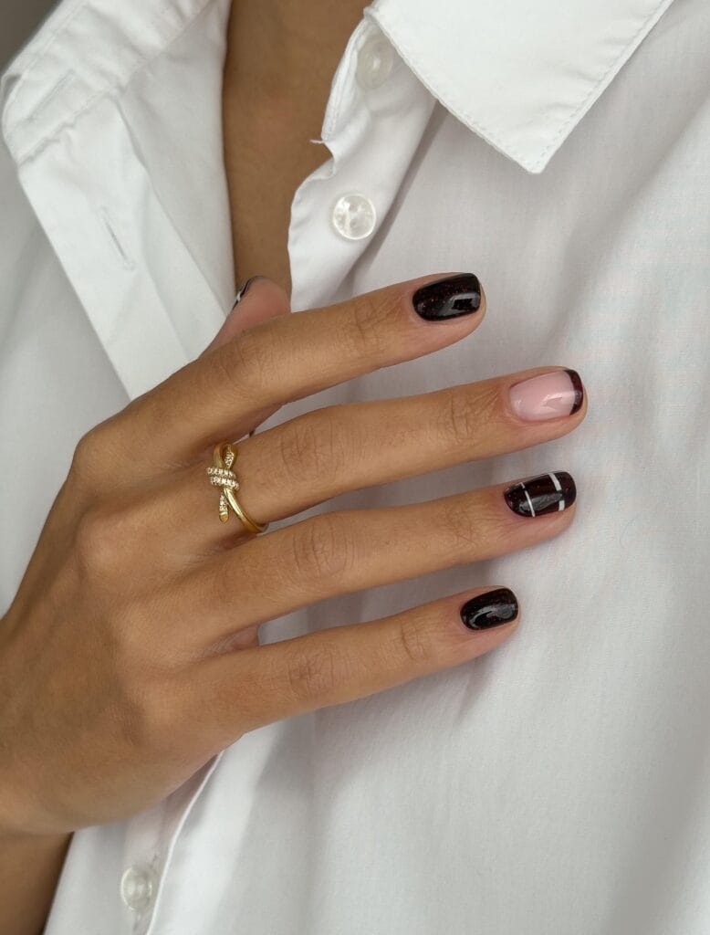 Short October nails with black cherry polish, a pink French tip, and fine white line art.