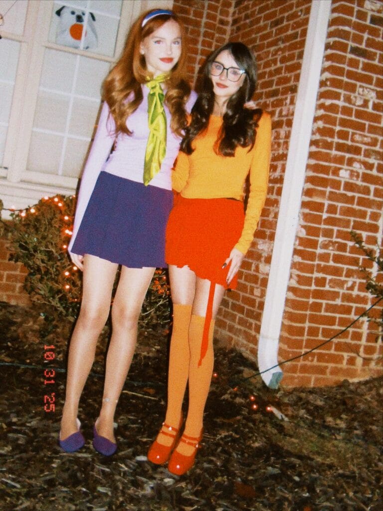 Daphne and Velma Halloween costumes for friends with purple separates, a green scarf, and an orange sweater
