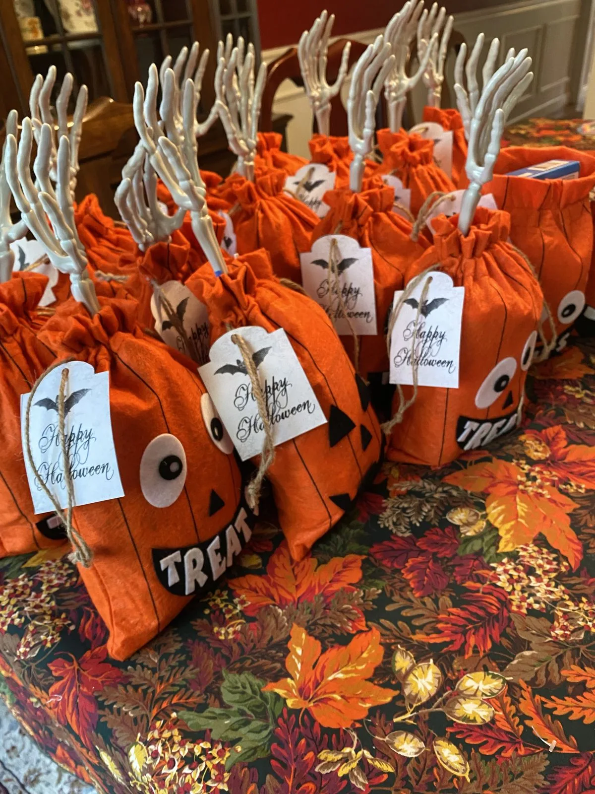 Halloween party favors in orange pumpkin bags with skeleton hands and "Happy Halloween" tags
