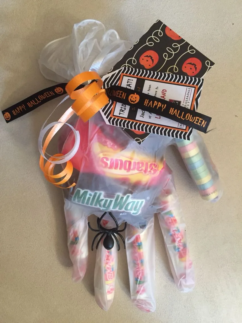 Clear glove Halloween party favor filled with candy, a plastic spider, ribbons, and Halloween tags