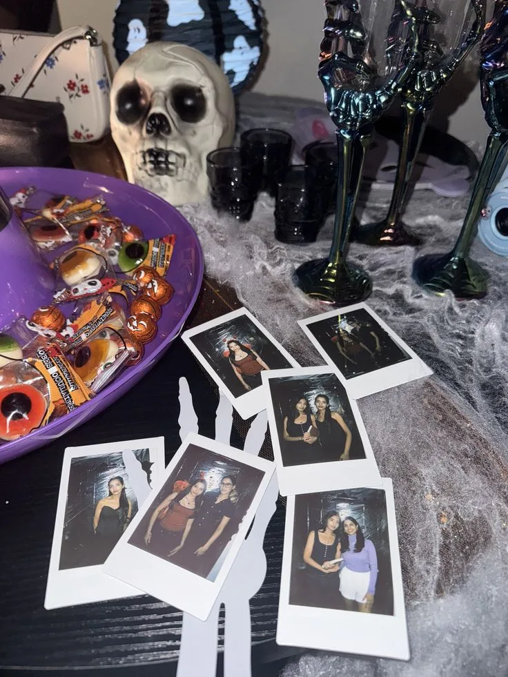 Halloween party table with instant photos, skull decor, black cups, candy, and skeleton-stem glasses
