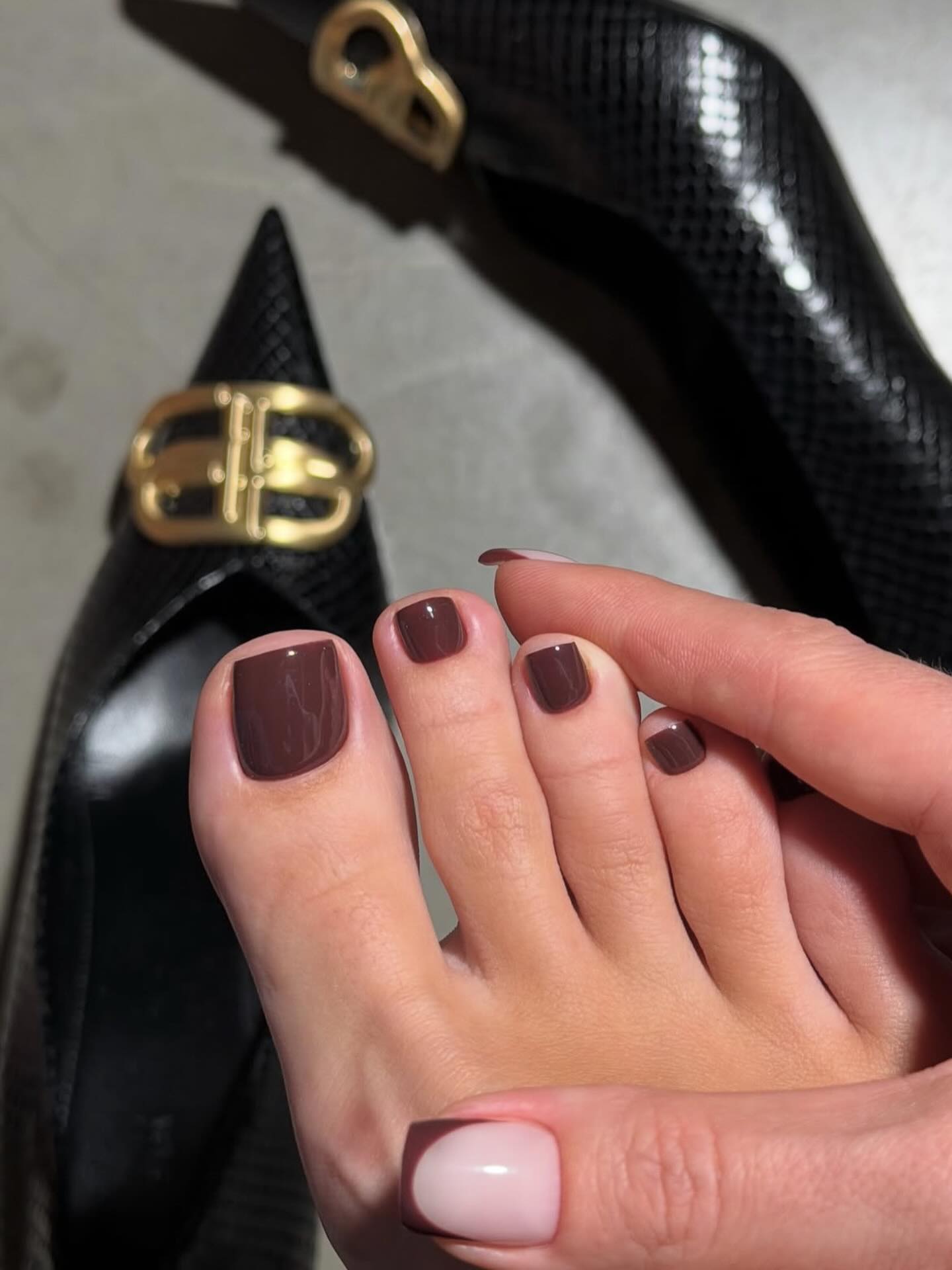 Brown fall pedicure with short square toenails beside black shoes with gold buckles.