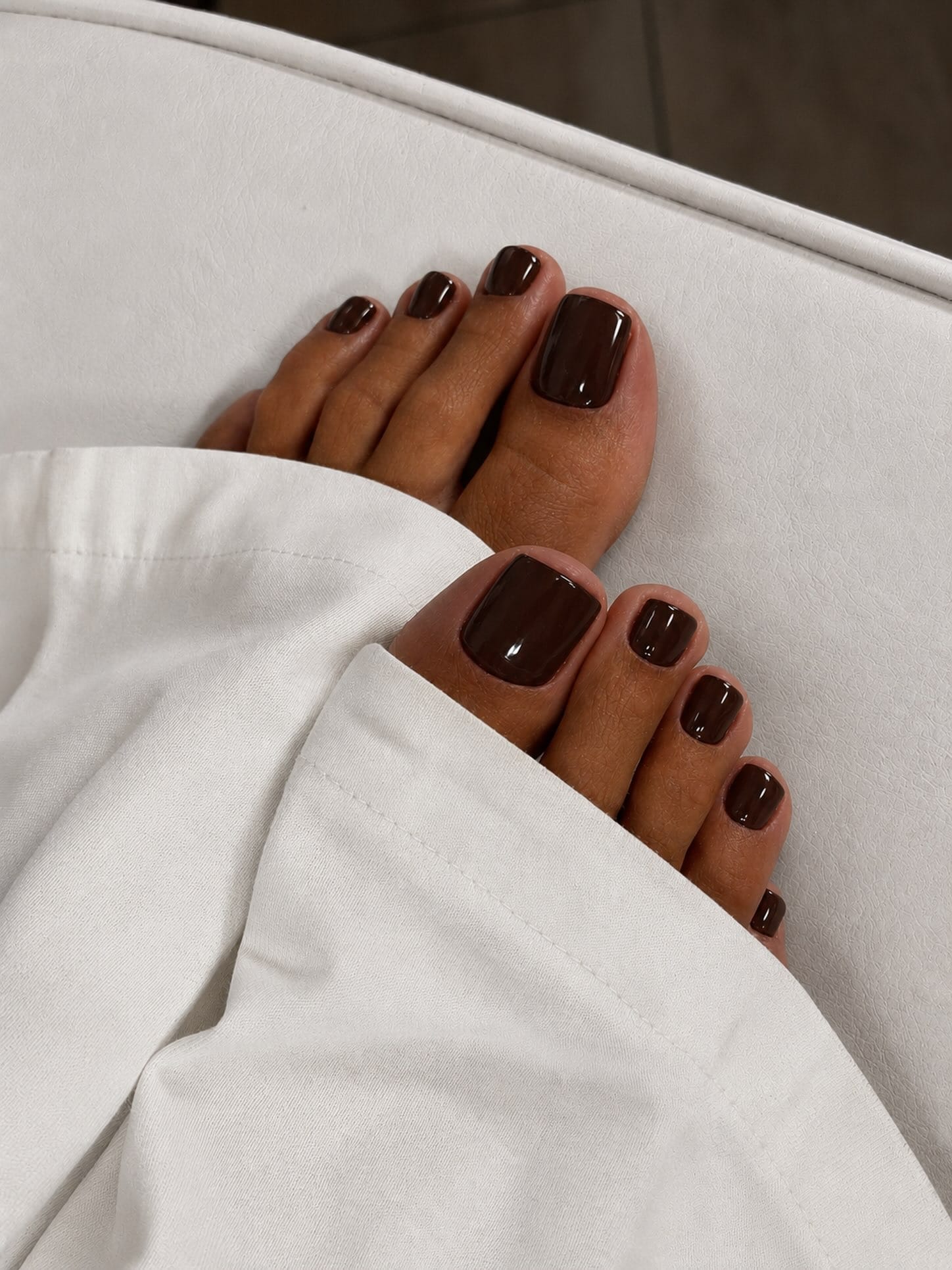Glossy espresso brown toe nail color for fall, shown with white trousers.