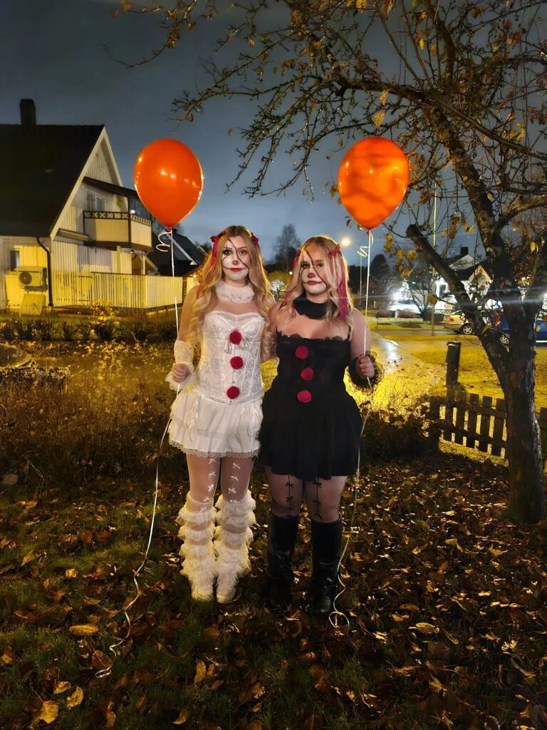 Best friend clown Halloween costumes with black and white dresses, red pom-poms, face paint, and orange balloons.