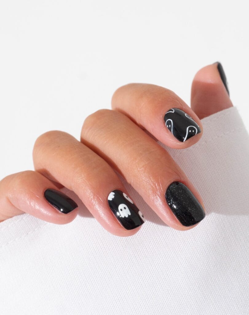 short spooky nails in glossy black with white ghost accents and one black glitter nail
