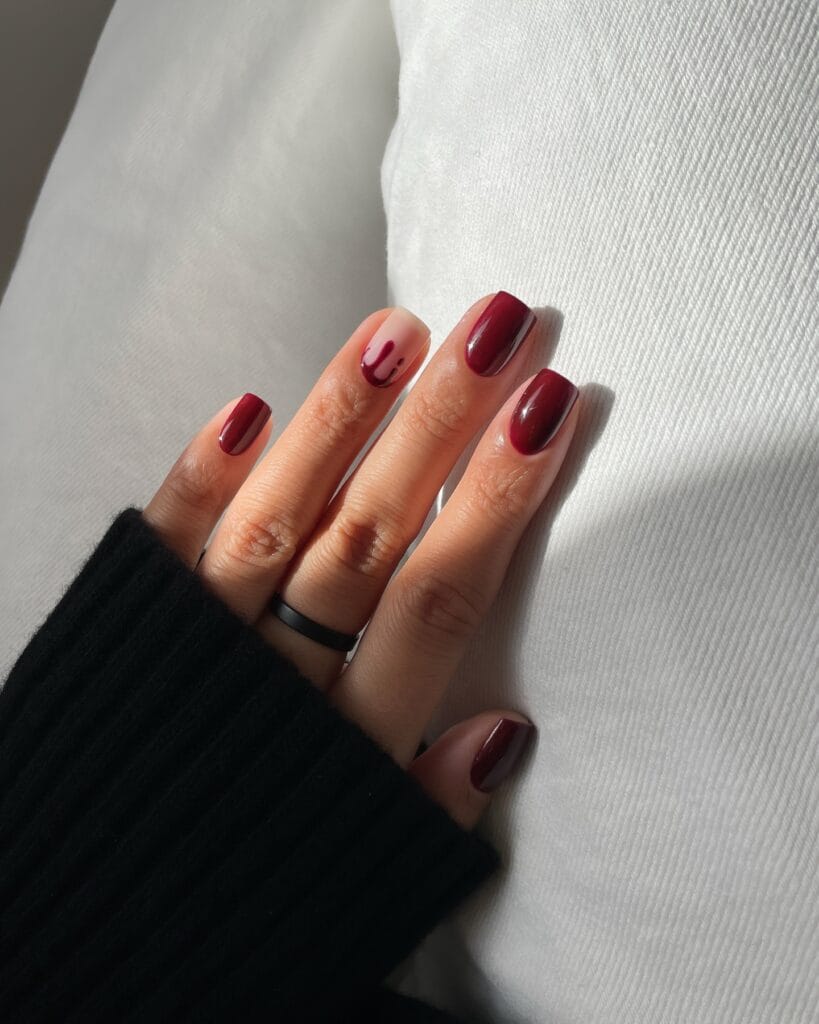short Halloween nails with burgundy ombré polish and one nude accent nail with a red drip design
