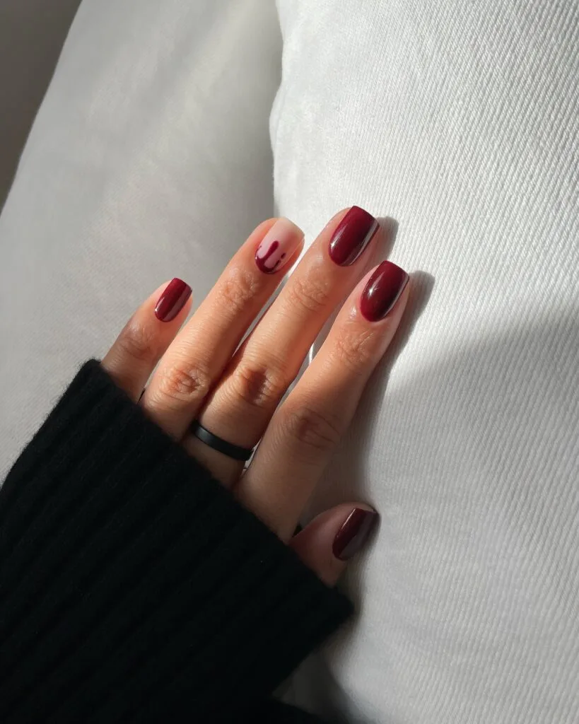 short Halloween nails with burgundy ombré polish and one nude accent nail with a red drip design