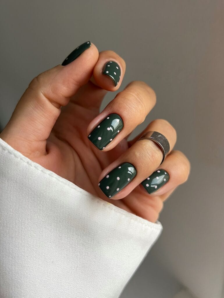 Square autumn nails with glossy forest green polish and small, widely spaced pale pink polka dots.
