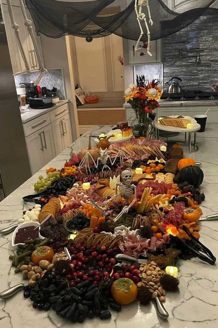 Halloween grazing table with meats, cheeses, fruit, crackers, pumpkins, candles, and small skeletons
