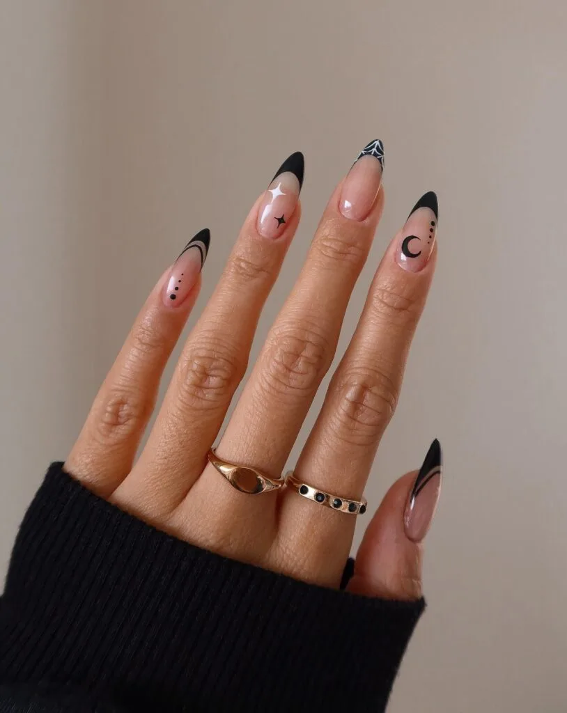 Witchy black French tips on nude almond nails with a crescent moon, stars, dotted trails, and a white web.