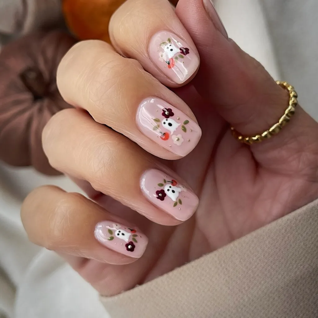 short Halloween nails in pale pink with tiny ghost art, floral accents, and mini orange details