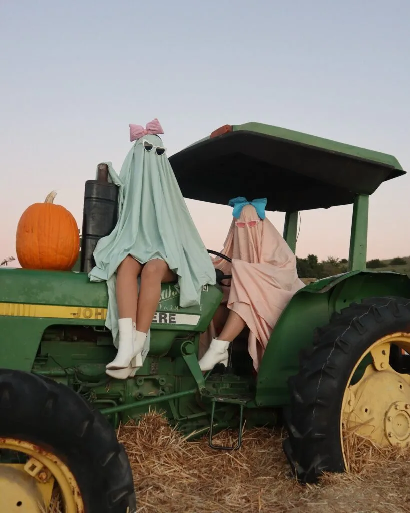 Pastel ghost Halloween costumes for best friends with pink and mint sheets, oversized bows, sunglasses, and white boots.