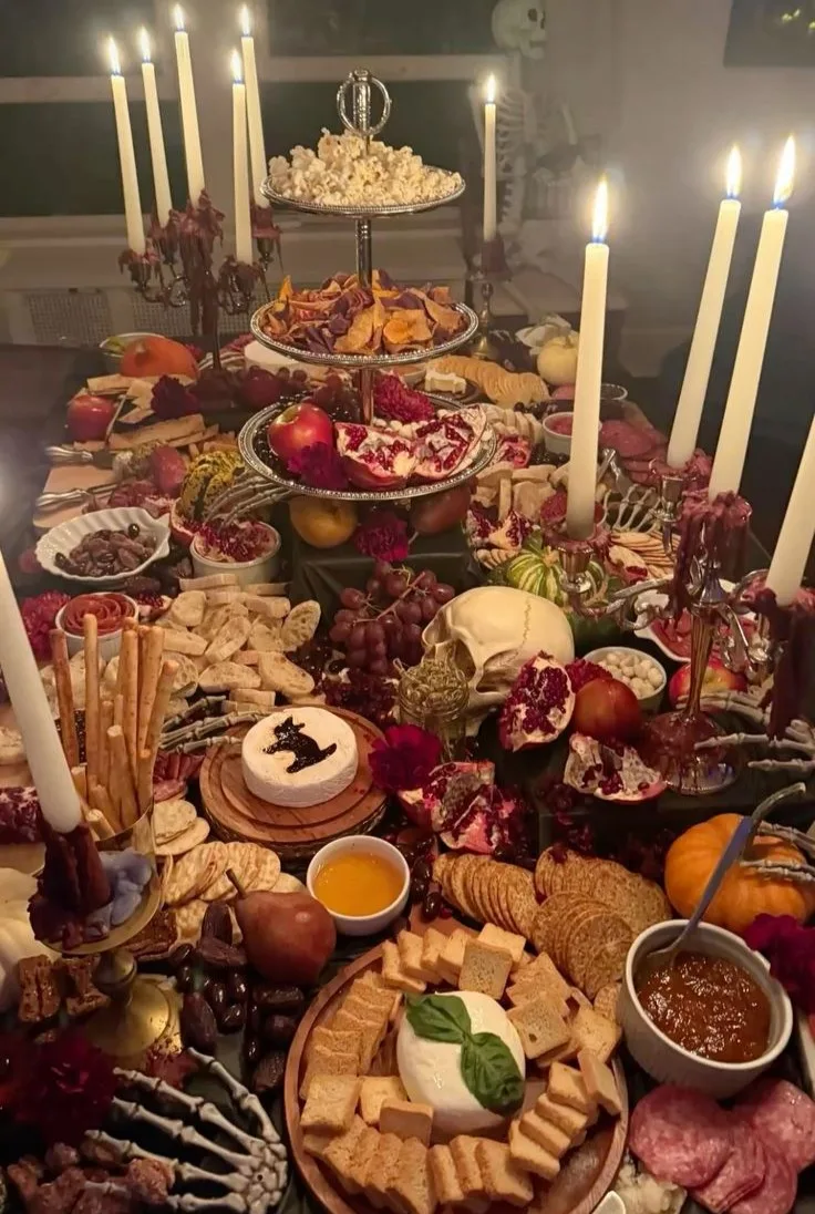 Halloween grazing table with candles, skull decor, pomegranates, cheeses, crackers, and charcuterie
