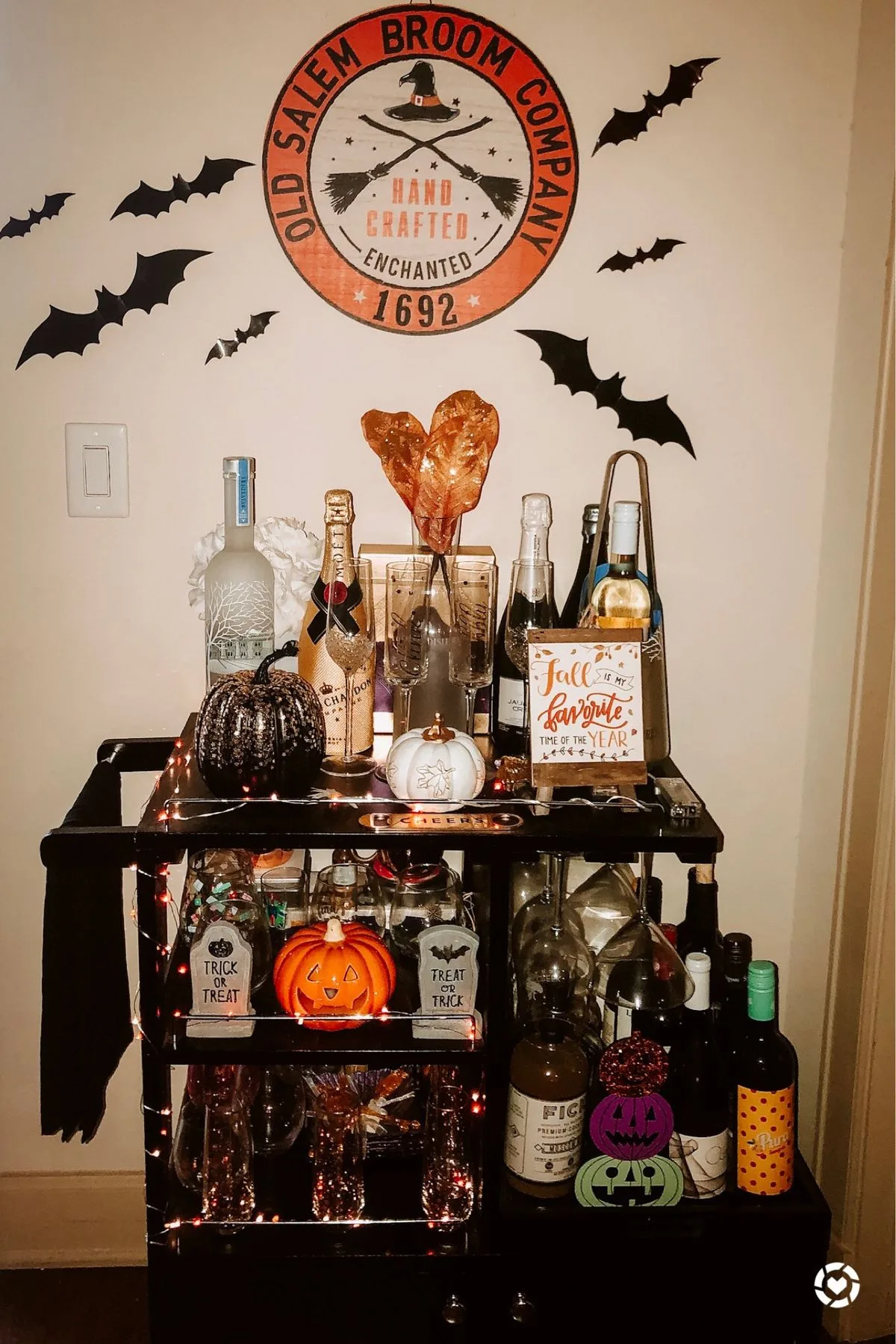 Halloween bar cart with bottles, pumpkins, bats, string lights, and an "Old Salem Broom Company" sign
