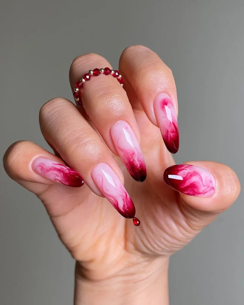 Pink and wine-red marbled Halloween nails with dark almond tips and a dangling red teardrop charm.