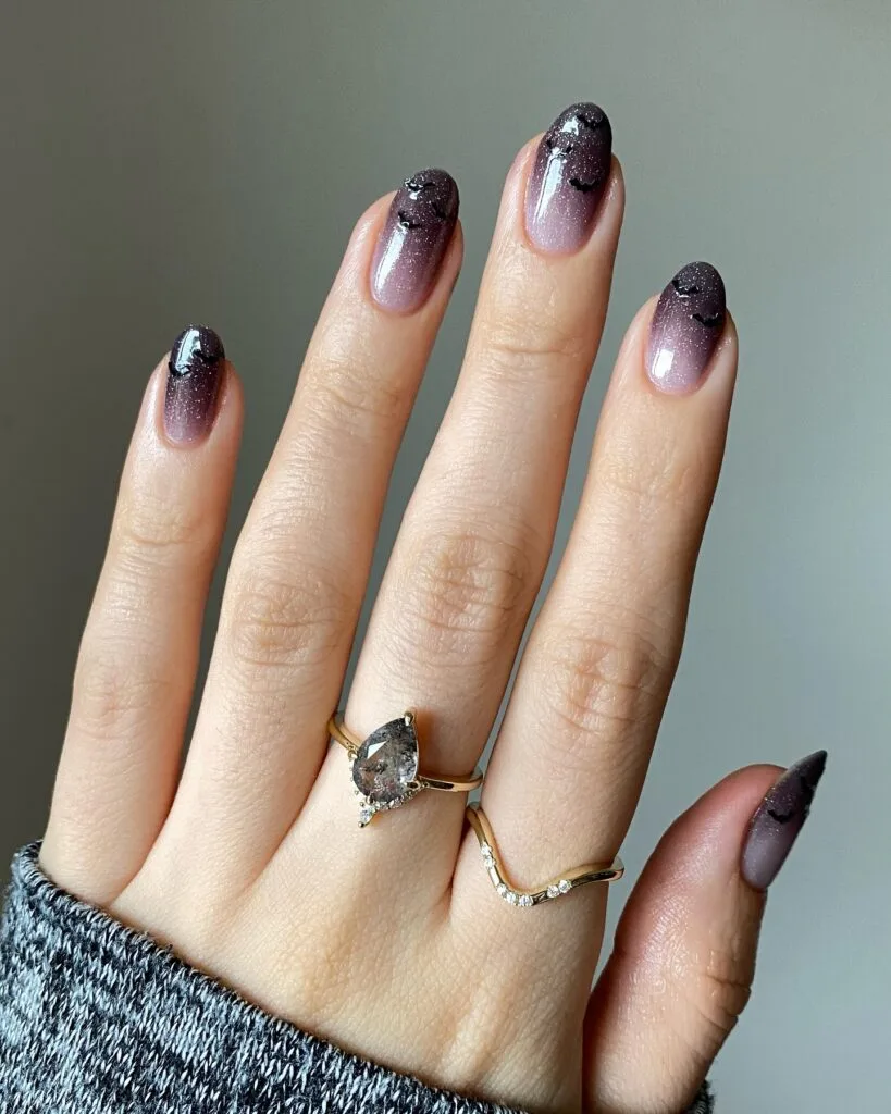 Shimmery mauve Halloween nails fading to deep plum at the tips, with tiny black bats on oval shapes.