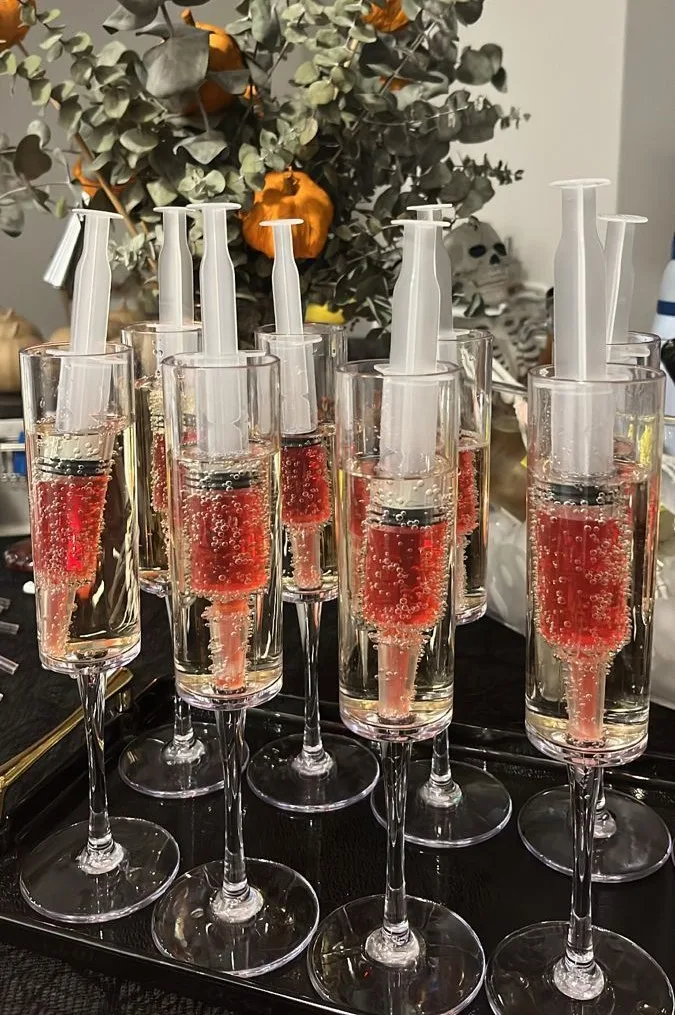Halloween drink station with champagne flutes holding red syringe-style shots
