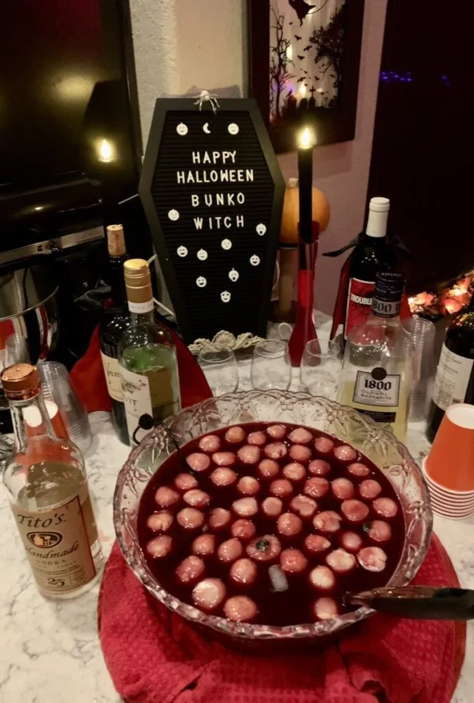Halloween punch station with red punch, floating eyeball-shaped ice, bottles, and "Happy Halloween" sign
