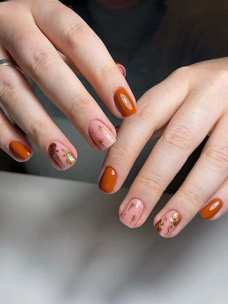short Halloween nails with glossy orange polish, blush accent nails, and gold stars and pumpkin details
