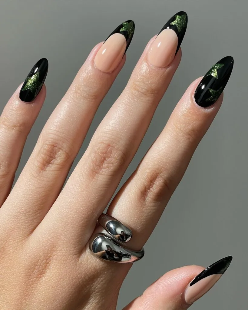 Long almond witchy nails with green glitter stars over glossy black nails and black French tips.