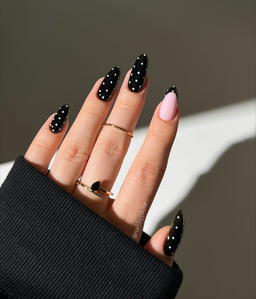 Black autumn nails with white dots and a pink French accent.
