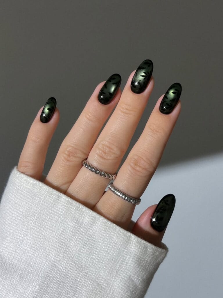 Dark green October nail ideas with black botanical art, cat-eye shine, and almond shapes.
