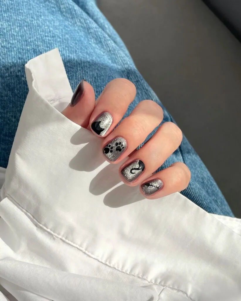 short spooky nails with silver glitter polish, black cat silhouettes, and a paw print accent