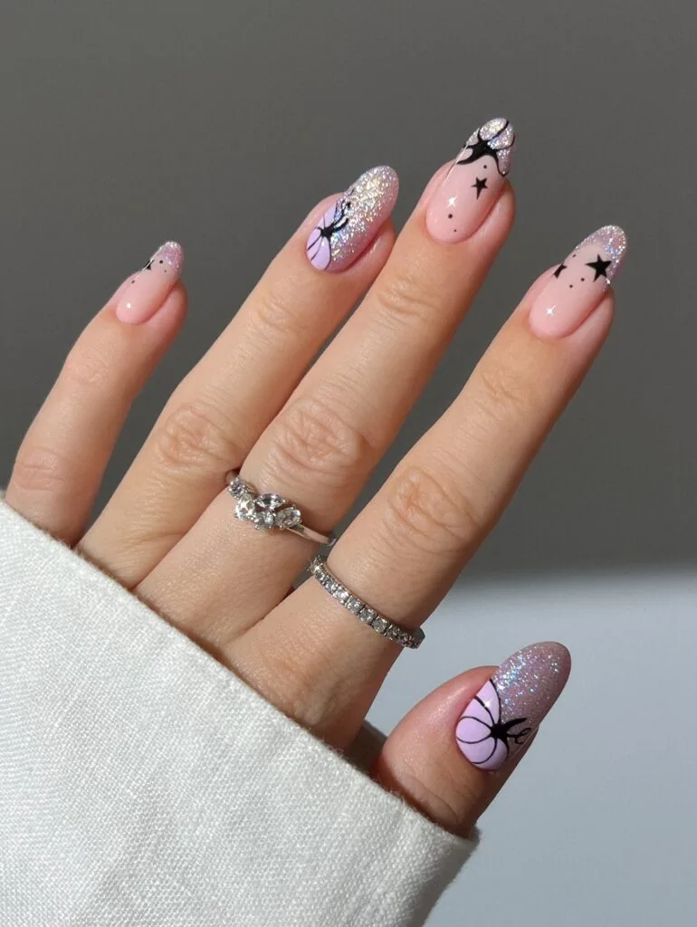 Pink Halloween nails with lilac pumpkins, black stars, and sparkling glitter French tips on almond shapes.