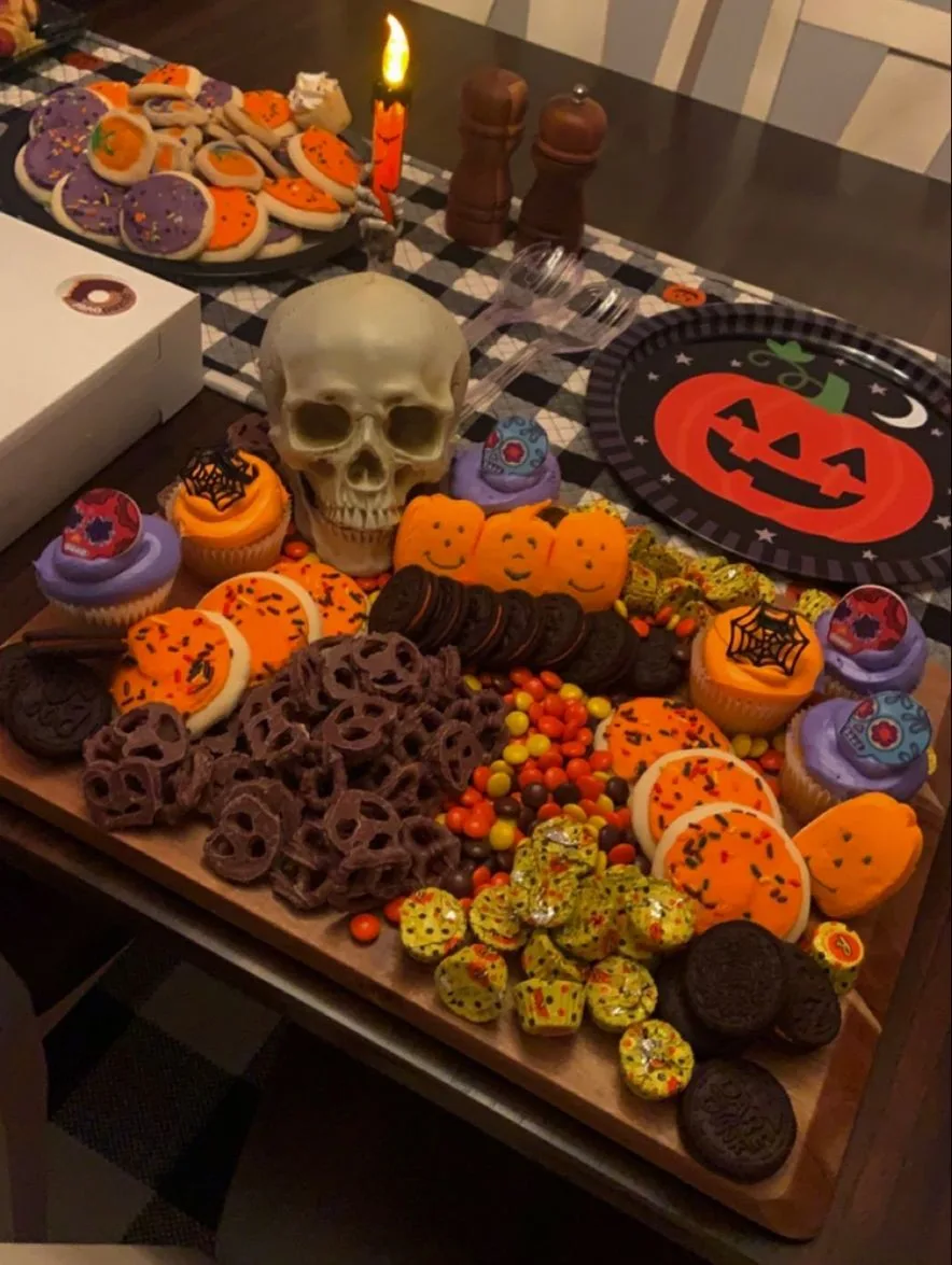 Halloween dessert table with orange cookies, cupcakes, candy, chocolate pretzels, and a skull
