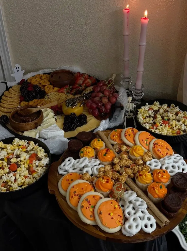 Halloween dessert table with popcorn, cookies, cupcakes, fruit, cheese, cobwebs, and candles
