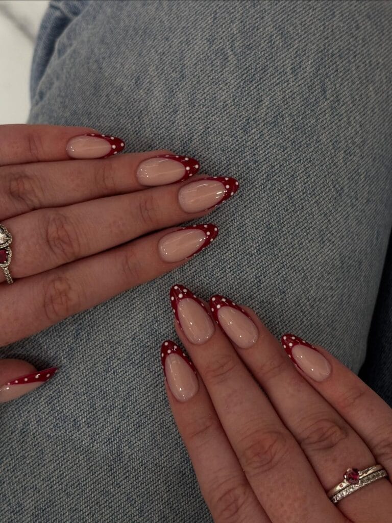 Almond fall polka dot nails with glossy nude bases and deep red French tips covered in white dots.
