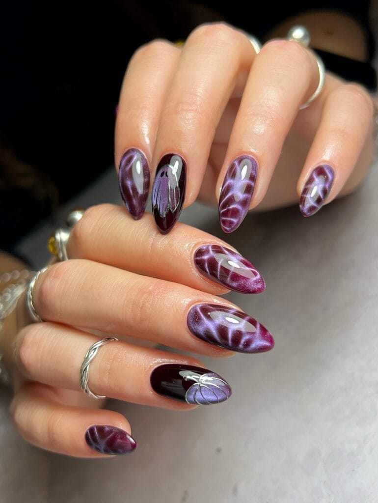 Purple fall nails with cat-eye swirls, a ghost accent, pumpkin nail art, and glossy almond shapes.
