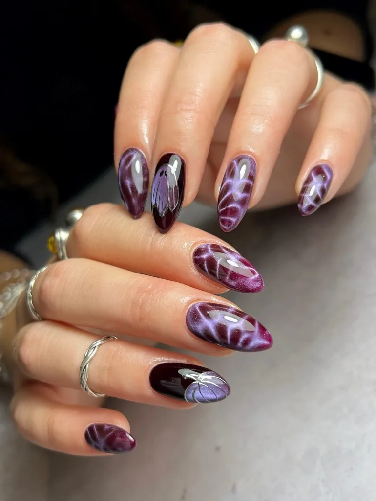 Purple fall nails with cat-eye swirls, a ghost accent, pumpkin nail art, and glossy almond shapes.
