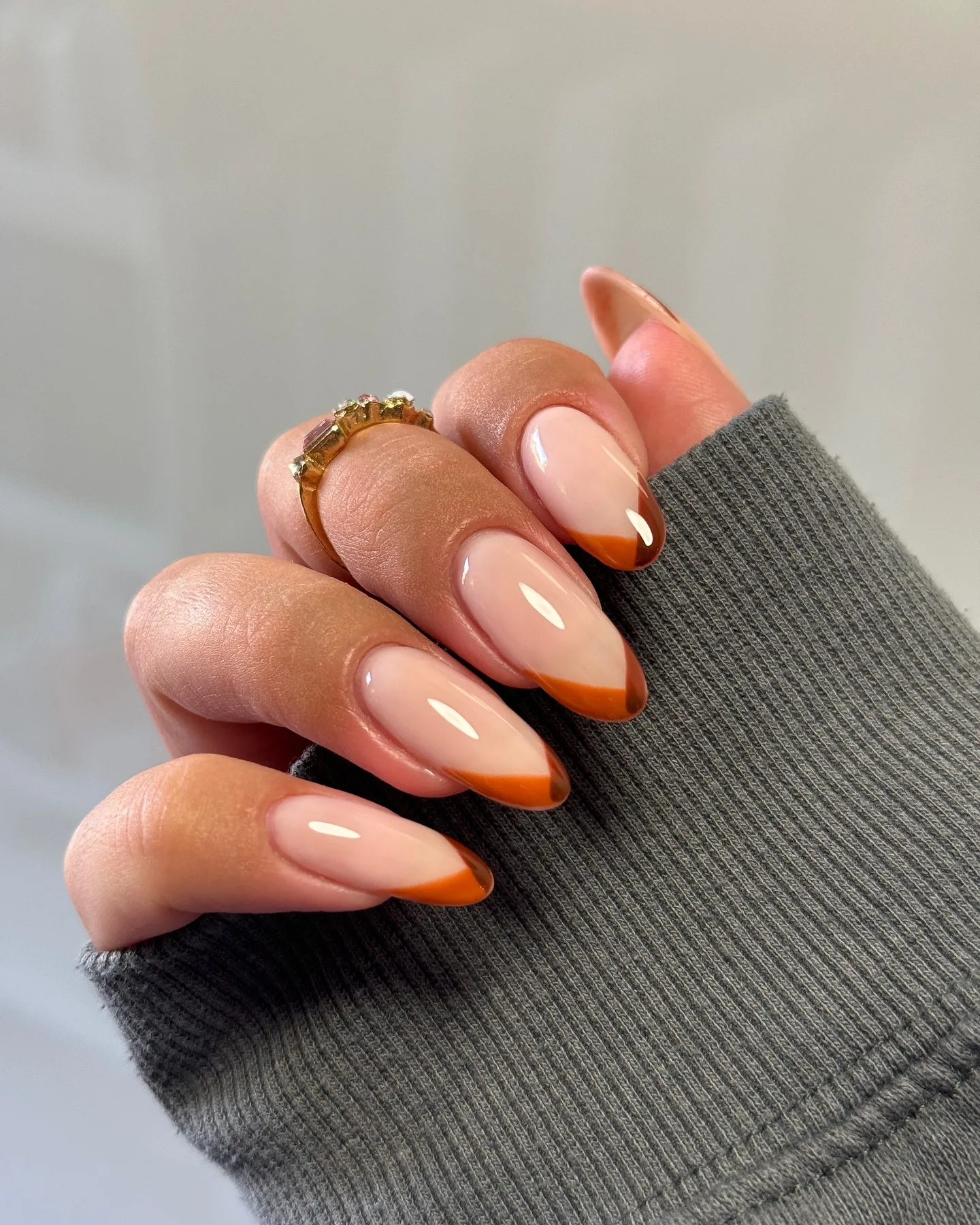 Almond fall nails with a sheer nude base and burnt orange V-shaped French tips edged in brown
