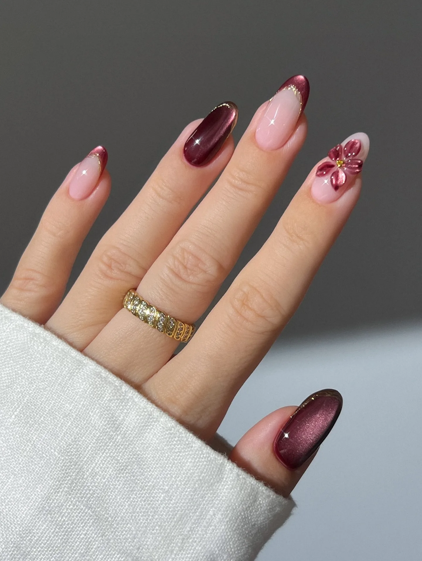 Almond autumn nails mixing burgundy velvet cat-eye, gold-lined French tips, and a 3D flower accent